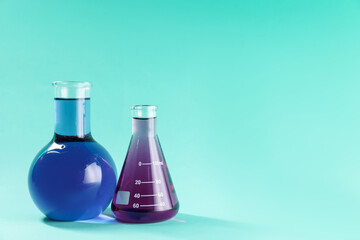 Laboratory glassware with colorful liquids on turquoise background. Space for text