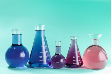 Laboratory glassware with colorful liquids on turquoise background