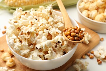 Tasty popcorn and corn kernels on white table, closeup