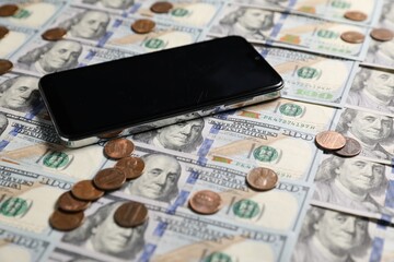 Smartphone and coins on dollar banknotes as background, closeup