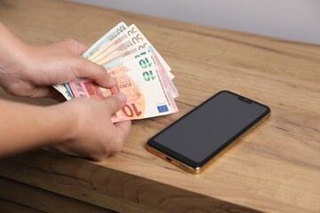 Woman with money and smartphone at wooden table, closeup