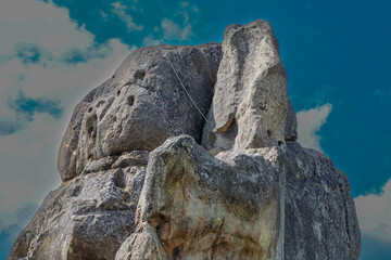 ​A massive, monolithic rock under a blue sky with clouds showcases natural power and strength....