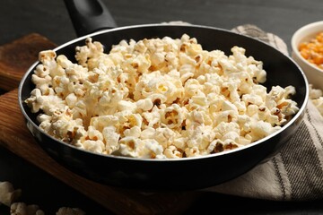 Tasty popcorn in frying pan on black table, closeup