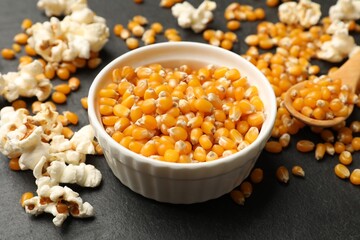 Corn kernels and tasty popcorn on black table, closeup