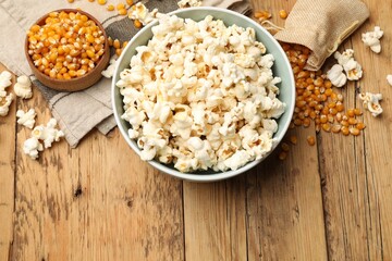 Tasty popcorn and corn kernels on wooden table, flat lay. Space for text