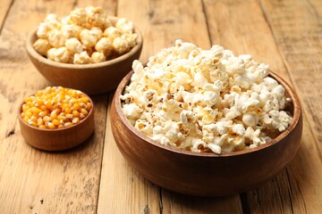 Tasty popcorn and corn kernels on wooden table, closeup