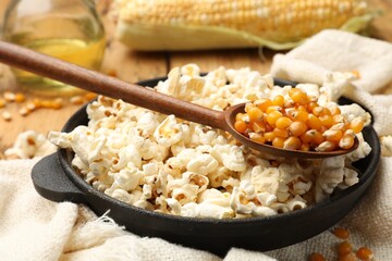 Tasty popcorn, corn kernels, oil and towel on wooden table, closeup