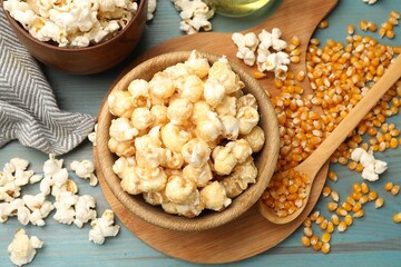 Tasty popcorn and corn kernels on blue wooden table, flat lay