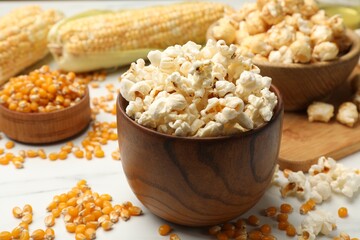 Tasty popcorn and corn kernels on white table, closeup