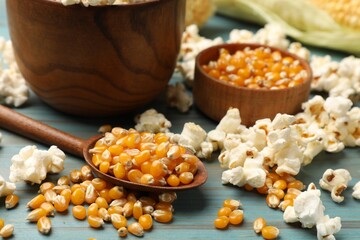 Corn kernels and tasty popcorn on blue wooden table, closeup