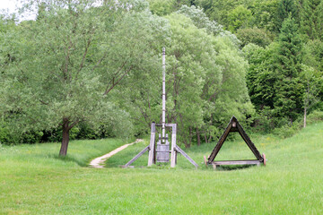 A picturesque rural scene with a traditional wooden well and another structure on a green meadow. A...