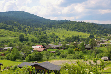 ​A rural Carpathian landscape filled with the greenery of forested mountains and cozy houses in the valley. The bright sun illuminates the hills and creates a harmonious atmosphere of peace and nature