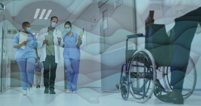 Walking medical team holding clipboards in hospital hallway, with patient in wheelchair using phone