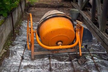 A small orange concrete mixer stands at a construction site