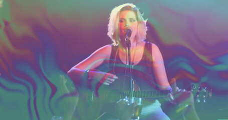 Strumming teen musician singing on stage, with acoustic guitar, microphone stand and stage lights