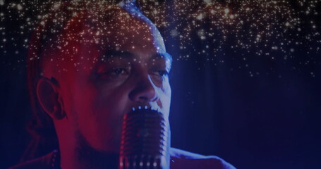 Singing performer with braids behind vintage microphone on stage under colored sparkling lights