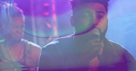 Singing singer wearing casual shirt gripping microphone on concert stage, with drum kit and trusses