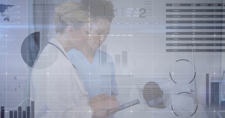 Senior physician and nurse reviewing medical data in clinic hallway, using tablet and stethoscope