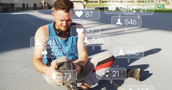 Adjusting prosthetic leg, man sitting on blue track wearing sportswear, floating social media icons