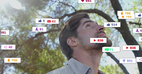Standing adult man wearing button-down shirt in park under trees, with floating notification icons