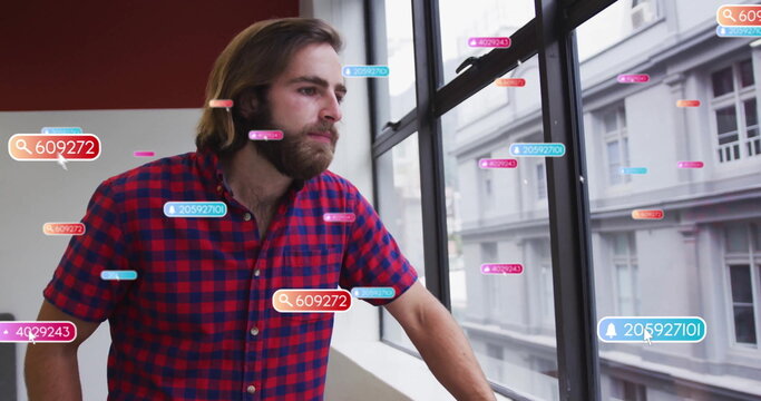 Leaning plaid-shirted man on windowsill gazing out window in office with data tags and search icons