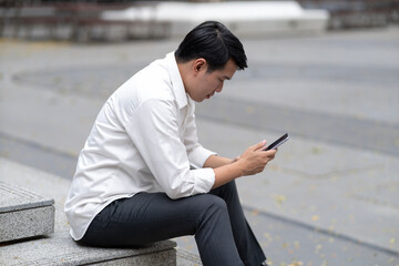 Asian adult man using smartphone outdoors focused communication technology business casual public space digital connection daily routine