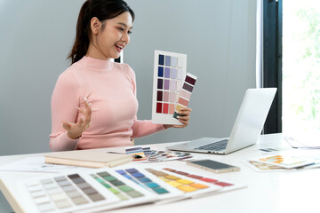 Asian adult woman designer discusses color palette selection creative project online video meeting laptop use modern office workspace bright environment