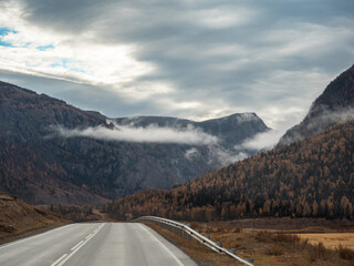 Scenic Road Through Mountains Landscape in Autumn Cloudy Day. Road Leading to Mountains with Fog in...