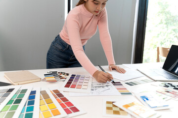 Asian adult woman designer selecting color palettes planning interior decor project creative modern office studio