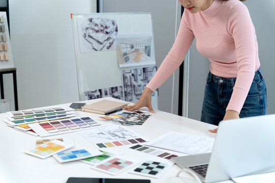 Asian adult designer selecting color swatches architectural blueprints for modern interior project planning professional office studio workspace