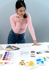 `Asian woman designer architect professional working office selecting color palettes architectural plans project inspiration creative focused studio desk planning concentration materials`
