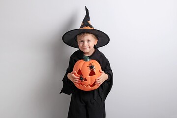 Child in witch costume holding carved pumpkin with playful expression for Halloween celebration on...