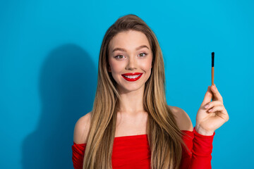 Obraz premium Charming young woman in red outfit holding a brush against a vibrant blue background while smiling cheerfully.