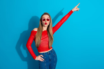 Stylish young woman in red top striking a playful pose against a vibrant blue background