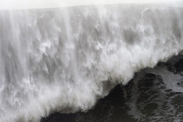 Turbulent ocean wave crashing, spraying white foam against dark sky, revealing powerful maritime...