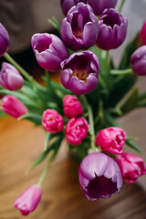 Close-up of vibrant pink and purple tulips in a glass vase. Fresh spring flowers with green leaves create a lively, cheerful, and romantic mood. Perfect for floral decoration and celebration