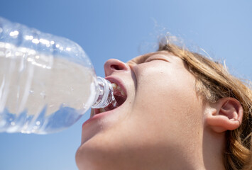 Teenager enjoying fresh water from a plastic bottle, soaking in the summer sun while staying...