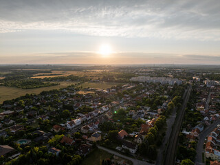 Naklejka premium Aerial view of Prague suburbs at sunrise, featuring fields, residential areas, and railway tracks bathed in the golden light of dawn