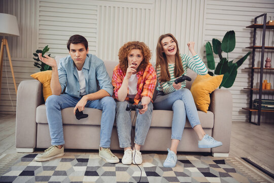 Three young friends enjoying video games together on a cozy living room sofa during a relaxing weekend