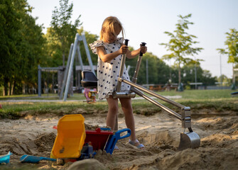 Young girl operating a metal digger in a sandbox, enjoying outdoor playtime on a sunny day at the...