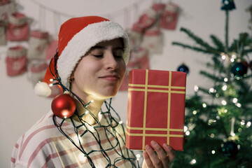 Teenage girl smelling Christmas gift near Christmas tree