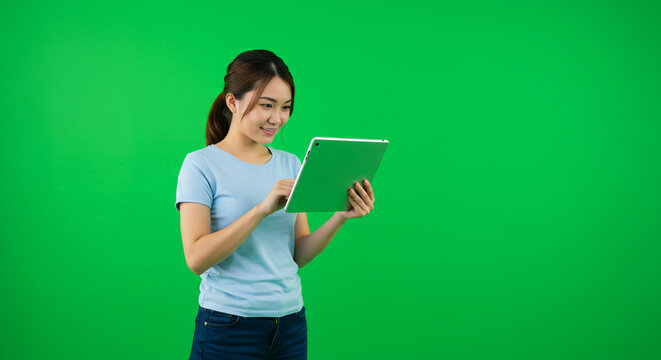 Smiling young woman interacting with a tablet on a vibrant green screen background, perfect for digital projects