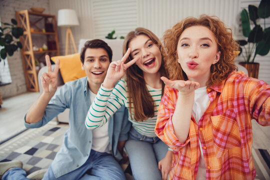 Three joyful young friends celebrate together in a brightly lit living room with casual attire and cheerful expressions - Powered by Adobe