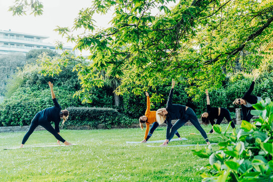Female yoga class in park. Group of diverse women doing stretching pose exercising together with instructor on green grass lawn. Sport activity for health, wellbeing, mental health. Selective focus