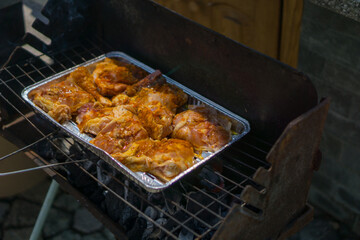 Grilled chicken pieces in an aluminum foil pan on a barbeque, concept of business grilling, summer holidays, family gatherings.