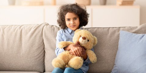 My Favorite Toy. Portrait of smiling beautiful African American girl embracing teddy bear, sitting...