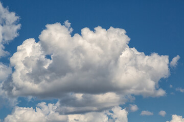 Large white cloud in the center of the frame against blue sky, cumulus white cloud on a bright sunny day in the blue sky, fluffy textured cloud in the sky.