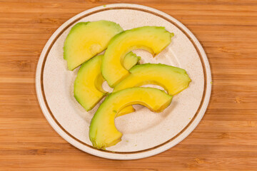Slices of avocado on saucer on wooden surface, close-up