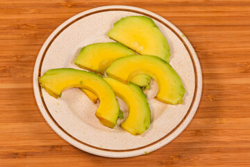 Slices of avocado on saucer on wooden surface, close-up
