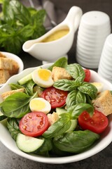 Tasty salad with croutons, tomatoes, cucumbers and basil on black table, closeup
